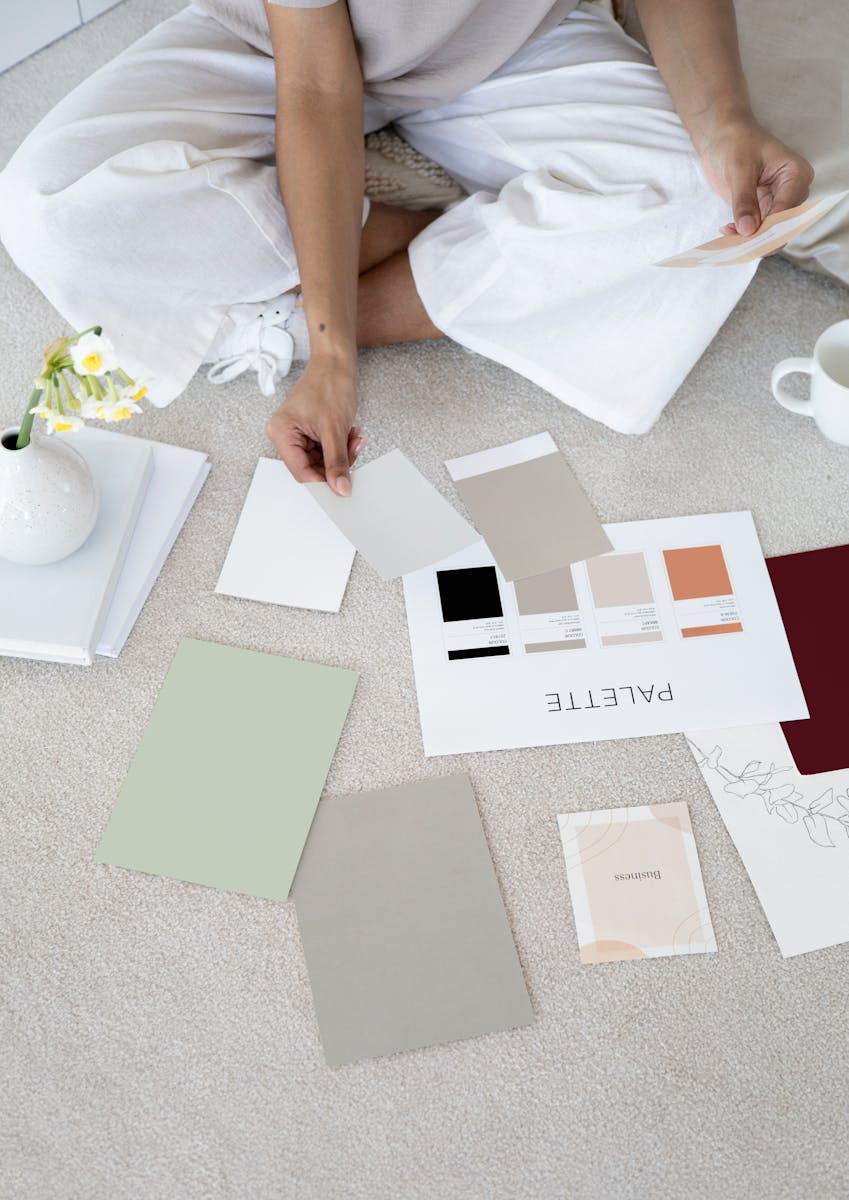 Photo by Anna Nekrashevich Designer sits on carpet with color palettes and samples, planning creative project.